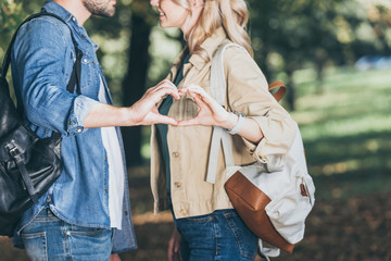 partial view of romantic couple showing heart sign made with hands in autumn park