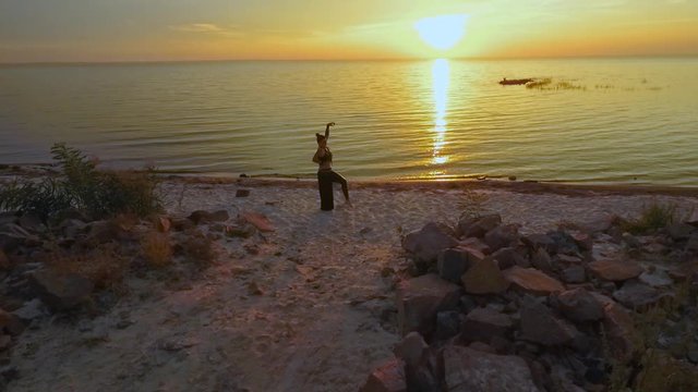 Beautiful girl dances on the sunset near water