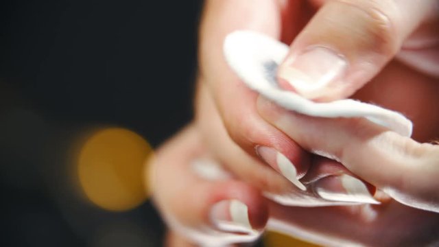 Cleaning blue color from long fingernail close-up 4K. Long shot of person's long blue fingernails in focus with black background decorative lights out of focus.