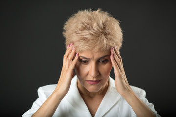 stylish woman in age with a short hairdo in a white jacket on a black background with a sad expression on her face