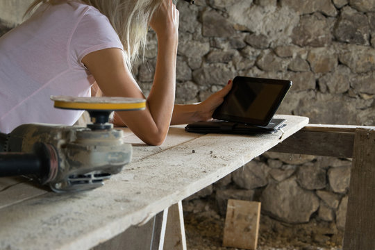 Crop view of female young adult with portable information device in hand makes a project  in a carpentry workshop - Powered by Adobe
