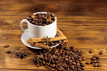 Coffee beans in white cup, cinnamon sticks and star anise on wooden table