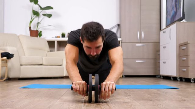 Sport at home - fit man doing exercises with an ab whell on the floor of his living room. Healthy lifestyle