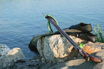 Spearfishing gear - fins, speargun  on a sea rock against blue sea background, space for text