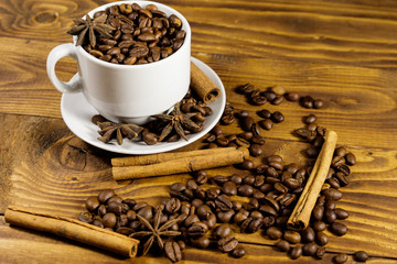 Coffee beans in white cup, cinnamon sticks and star anise on wooden table