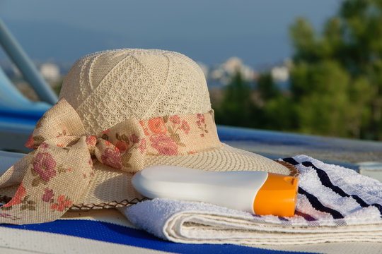 Close up of summer hat, towel and sun protection cream on a deck chair