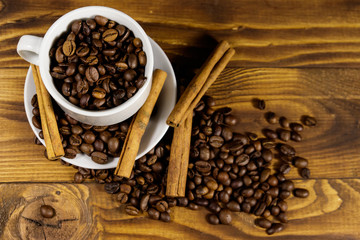 Coffee beans in white cup and cinnamon sticks on wooden table. Top view
