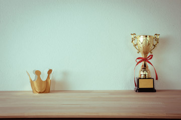 cardboard golden crown with champion golden trophy placed on wooden table.