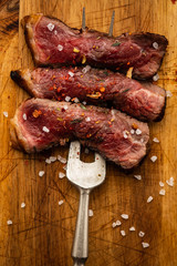 Slices of beef steak on meat fork on wooden cutting board.