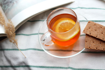 transparent Cup of tea with lemon, rye crispbread, a book, natural light, breakfast