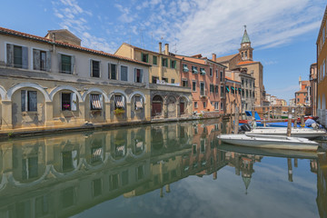 City landscape with canal, boats and colorful reflections on the water in the picturesque old town in Chioggia, Venice, Italy.
