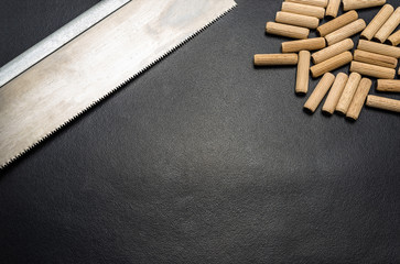 A lot of wooden pegs and hand saw for wood lying flat on a black background.