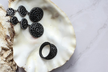 black ring and earrings with precious stones on a shell on the marble background
