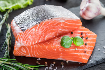 Fresh salmon fillets on black cutting board with herbs and spices.