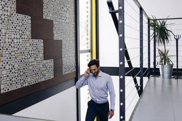 Handsome businessman talking on mobile phone and climbing on the stairs in modern office