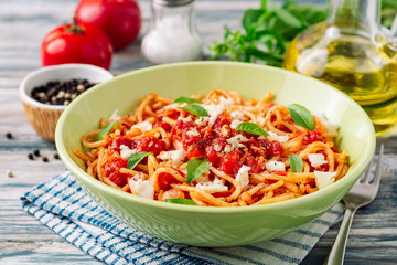Spaghetti pasta with tomato sauce, mozzarella cheese and fresh basil leaves on white-blue vintage wooden background. Selective focus.