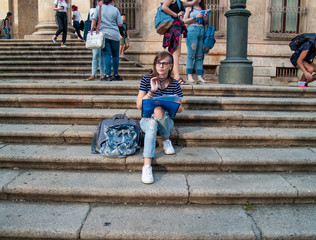 A teenage woman studying with a binder on the stairs of a university in a university campus