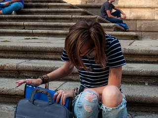 A teenage woman studying with a binder on the stairs of a university in a university campus