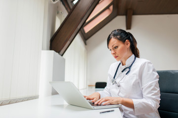 Serious female doctor working on laptop.