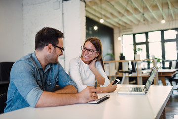 Two smiling colleagues talking in modern open space office.