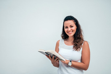 Beautiful young woman reading a book on isolated background. Looking at camera. Copy space.