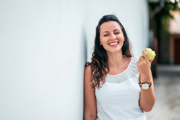 Young woman laughing and eating an apple outdoors.