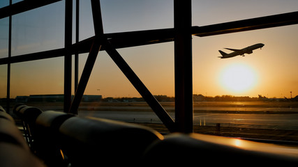 Silhouette of an airplane taking off at sunset at Beijing airport in the background of a window. © Довидович Михаил