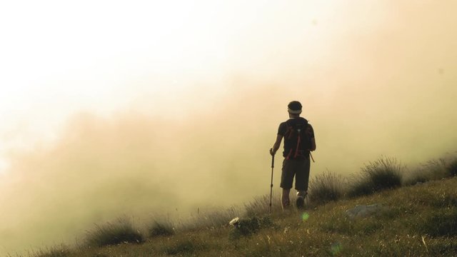 Young trekker man walking up the mountain in the fog with backpack, boots and trekking poles. Clouds and myst moving on the background. Abruzzo Italy.