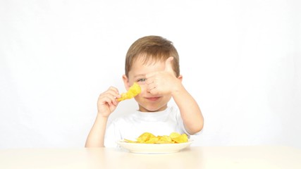 A child with pleasure eating potato chips sitting at a table on a white background