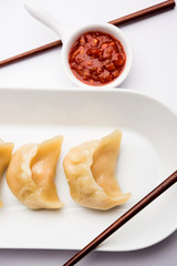 Dumpling momos food from Nepal or Ladakh served with red chilli chutney over moody background. Selective focus