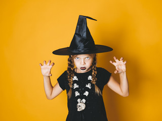 young halloween witch on orange background with black hat