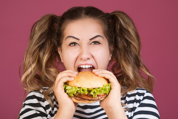 Teen girl holding the beef burger sandwich with happy face and hungry open mouth on isolated pink background. Fast food concept.