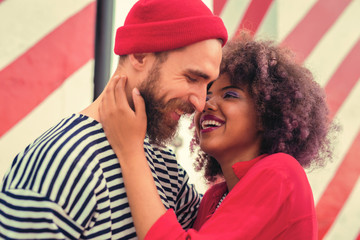 Nice joke. Cheerful young curly woman hugging her attractive bearded boyfriend and laughing at the...