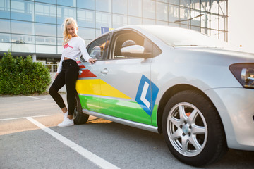 Female driving student standing next to a car