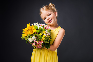 stylish smiling kid in yellow dress holding floral bouquet, isolated on grey