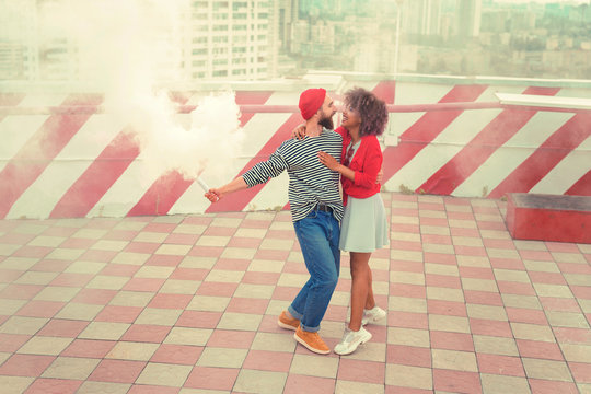 Dancing and smiling. Cheerful young loving couple smiling and feeling happy while dancing on the roof with smoke flare - Powered by Adobe