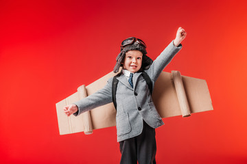 little emotional pilot in suit and cardboard plane wings with outstretched arms to fly isolated on...