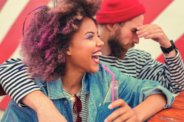 Loud laughter. Positive young woman laughing while her tired boyfriend having headache and feeling unwell after the party