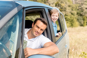 happy father and son riding car on nature and looking at camera