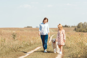 Fototapeta premium happy mother and daughter walking with golden retriever in field