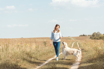 beautiful adult woman walking by field with retriever dog
