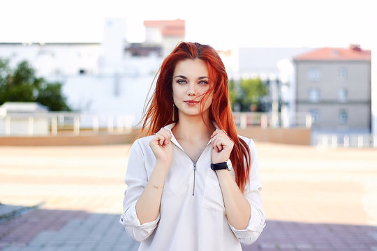 Red-haired teenage girl hold shirt collar with her hands. Natural ginger lady posing and looking at camera outdoors. Portrait of foxy beautiful caucasian woman.
