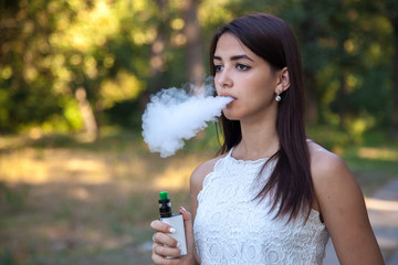 serious cute woman smoking e-cigarette in the park