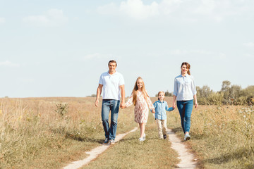 Naklejka na ściany i meble happy young family holding hands and walking by field