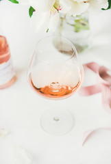 Fototapeta na wymiar Rose wine in glass, pink decorative ribbon, peony flowers over white background, selective focus, close-up. Summer celebration, wedding greeting card, invitation concept