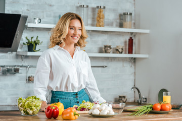 beautiful adult woman with various fresh vegetables on kitchen table looking away