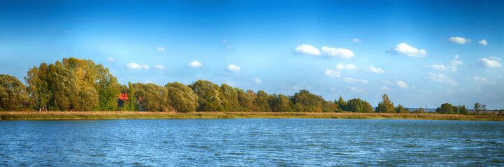 Panoramic shot of a beautiful summer countryside. River, forest and blue sky.