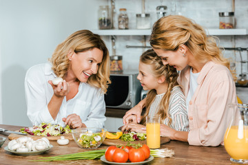 child cutting vegetables for salad with mother and grandmother at home and chatting