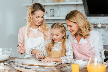 smiling little child cutting dough for cookies with mother and grandmother at home