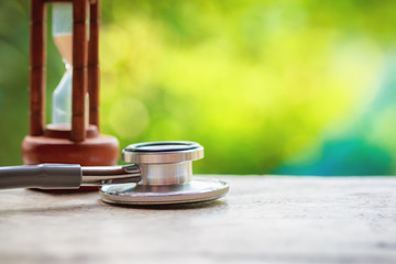 Health care check up. Stethoscope and hourglass on wooden table and Greenery Natural background....
